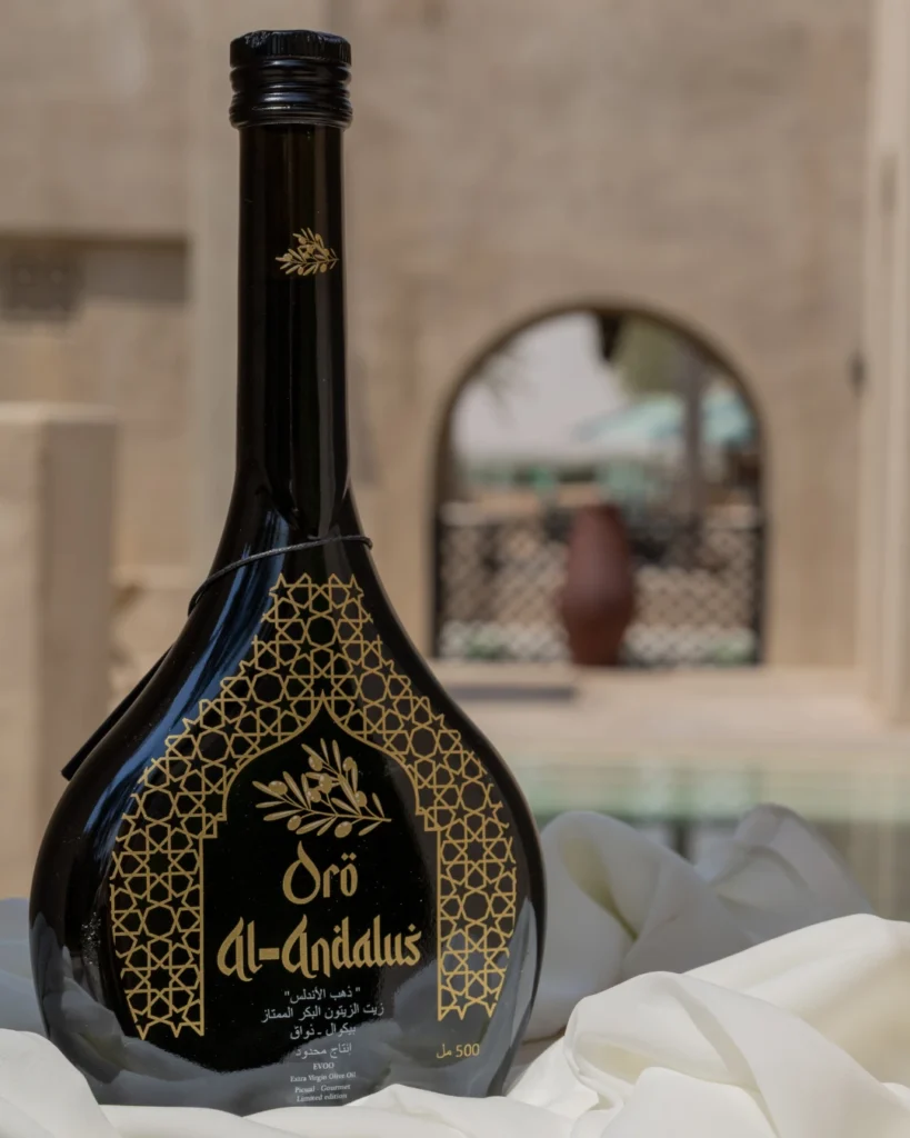 Oro Al Andalus Arabesca Extra Virgin Olive Oil 500ml black and gold bottle on white silk fabric with a traditional Moorish arch and clay pot in the background
