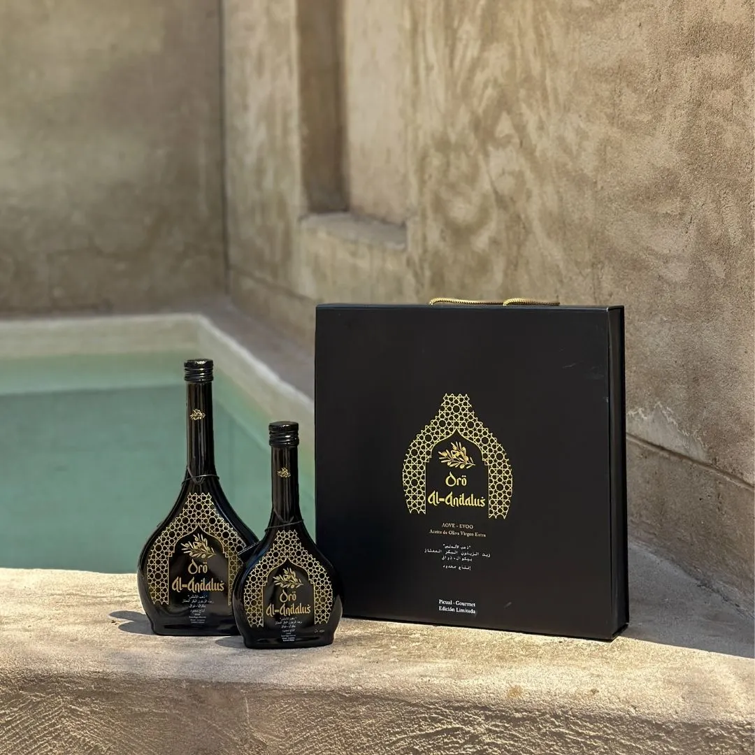 Oro Al Andalus Luxury Case with two Arabesca EVOO bottles in 250ml and 500ml, displayed on a stone ledge beside a traditional hammam pool with a teal water reflection